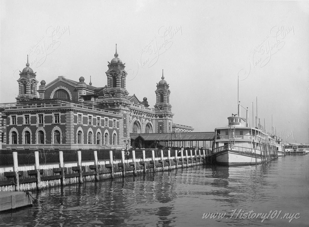 An exterior perspective of Immigration Station at Ellis Island, with ferry docked at the adjacent pier.