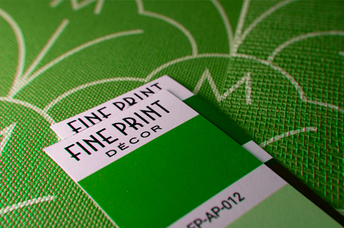 Closeup photo of a green, textured wallpaper sample with color chips laid on top for color matching